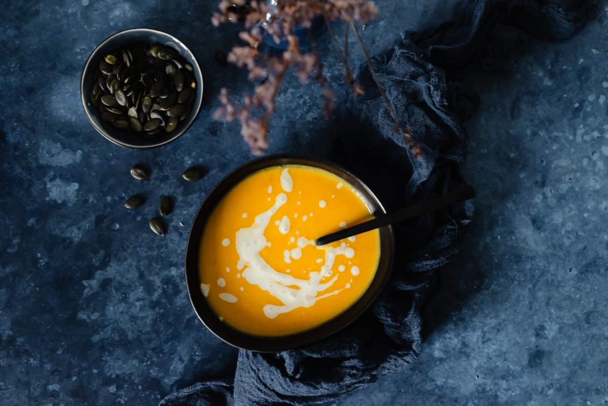 Herbstliche Kürbiscremesuppe vor blauem Hintergrund mit Kürbiskernen