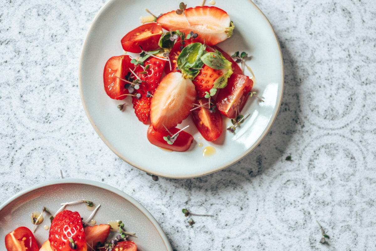 Tomatensalat mit frischen Erdbeeren auf hellen Fliesen fotografiert